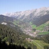 Paysage dans les Aravis avec un décor très montagnard, avec des sommets en fond des arbres un peu plus près et une vallée au centre