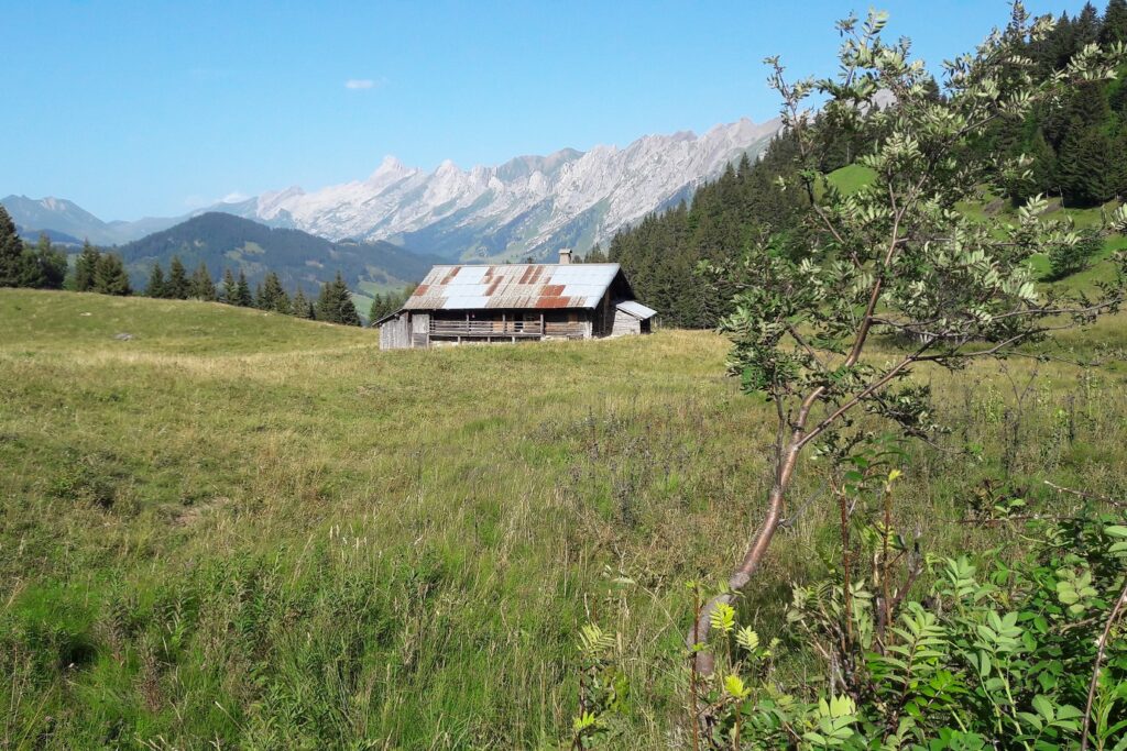 Paysage de montagne dans les Aravis, avec en fond des sommets et devant cela un bâtiment au sein de la montagne
