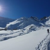 Groupe de randonneurs sur un sentier de randonnée avec en fond des sommets couverts de neige.