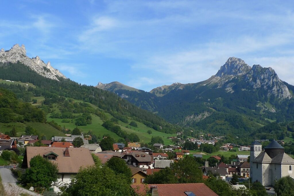Paysage d'un village dans le pays du Léman, encadré de sommets, d'arbres et de végétation, avec un soleil estival