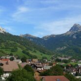 Paysage d'un village dans le pays du Léman, encadré de sommets, d'arbres et de végétation, avec un soleil estival