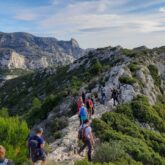 Groupe de randonneurs sur un sentier de randonnée sur des crêtes de montagnes encadré de végétation des deux côtés