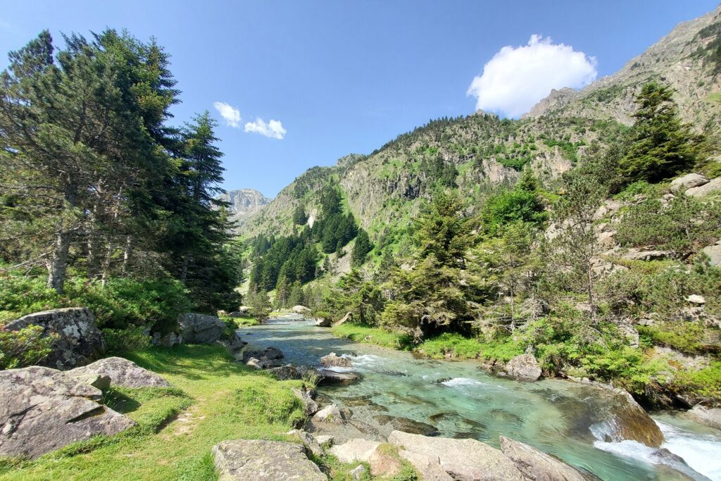 Paysage montagnard avec un cours d'eau en milieu d'image, avec des sentiers en bord de cours d'eau