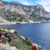 Groupe de randonneurs avec leur guide sur un sentier, flanc d'une falaise, avec la mer en contrebas