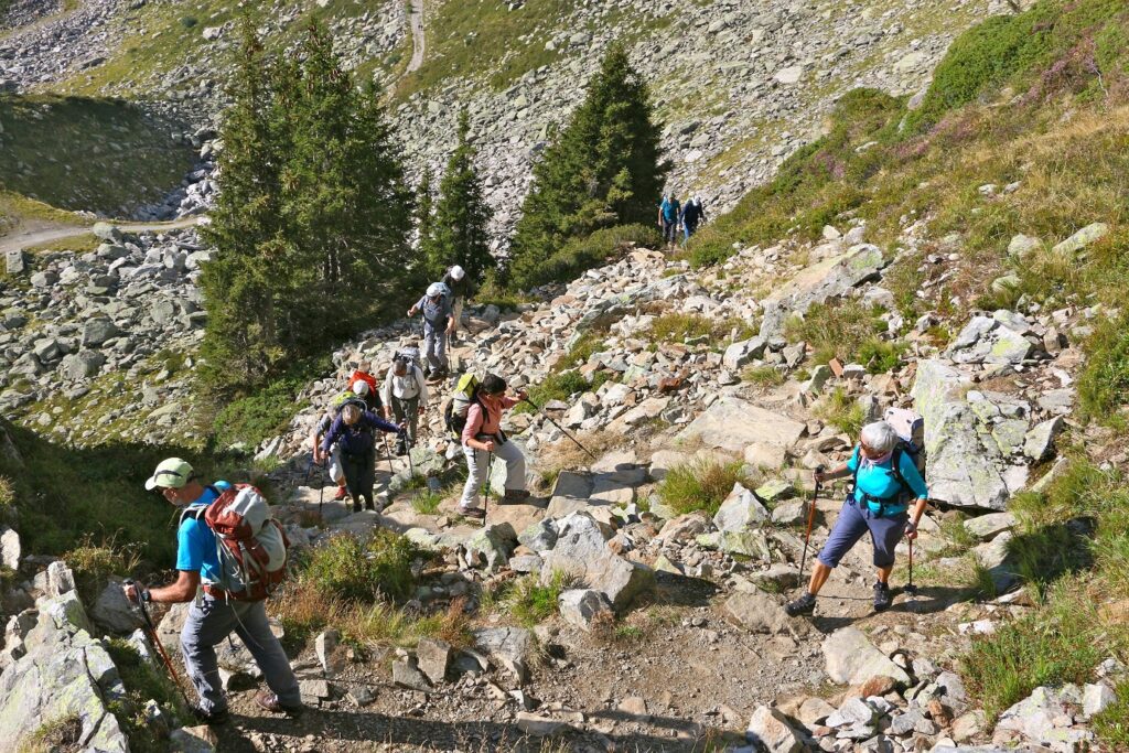 Groupe de randonneurs sur un sentier de randonnée avec beaucoup de cailloux en train de monter avec leur guide lors du tour du mont Blanc sud