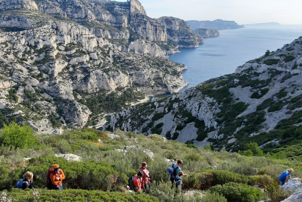 Groupe de randonneurs sur un sentier de randonnée en train de descendre à flanc de montagne vers les calanques.