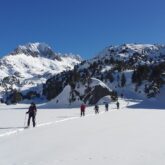 Groupe de randonneurs en raquettes sur un sentier de randonnée dans la neige, avec dans le fond de nombreux sommets