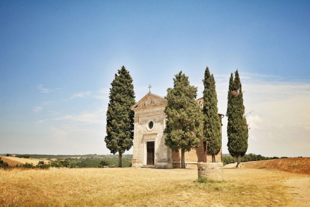 Paysage toscan d'une abbaye encadré par deux cyprès, dans un environnement isolé et très sec, avec de l'herbe jaunie