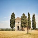 Paysage toscan d'une abbaye encadré par deux cyprès, dans un environnement isolé et très sec, avec de l'herbe jaunie
