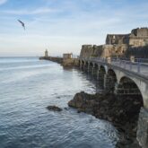Paysage jersey, une des îles au large de la Bretagne avec un pont sur la droite et des habitations et l'océan sur la gauche