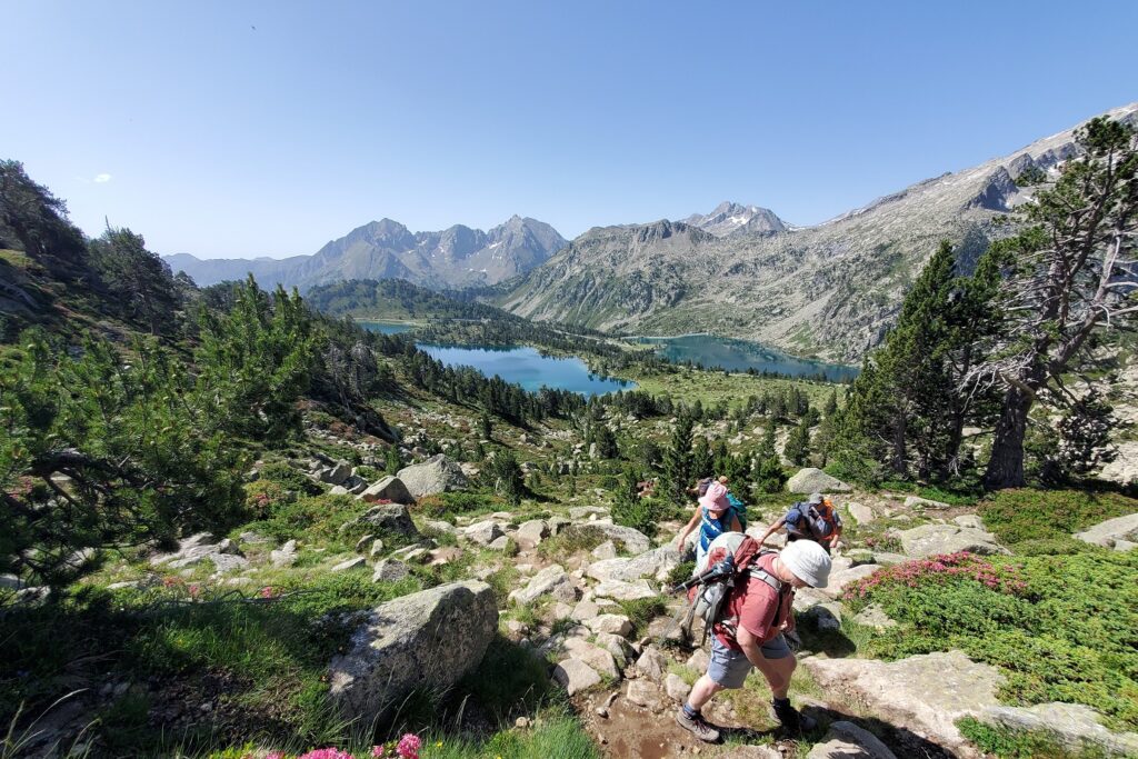 Groupe de randonneurs sur un sentier de randonnée avec en fond un lac de montagne et des sommets appartenant au massif du Néouvielle
