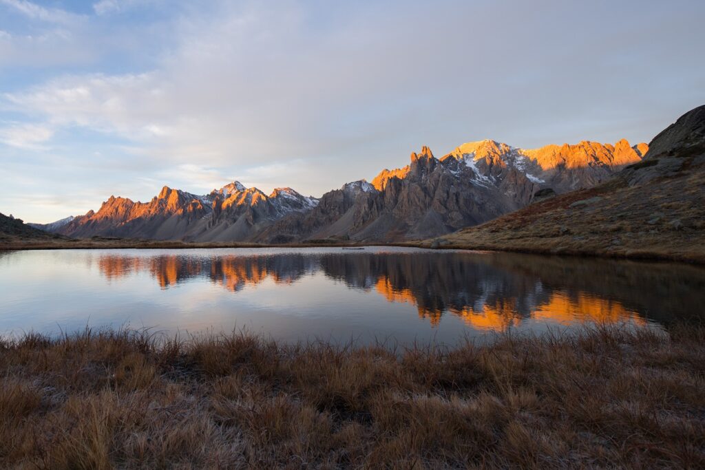 Paysage de montagne avec un lac au centre de l'image et des sommets en fond, avec le début du levé du soleil qui touche les sommets