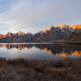 Paysage de montagne avec un lac au centre de l'image et des sommets en fond, avec le début du levé du soleil qui touche les sommets