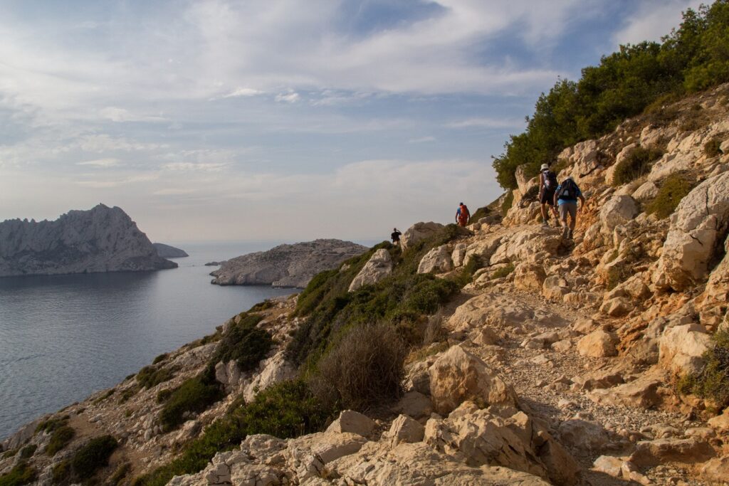 Paysage dans les calanques : un groupe de randonneurs sur un sentier avec en contrebas, sur la gauche, la mer