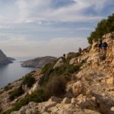 Paysage dans les calanques : un groupe de randonneurs sur un sentier avec en contrebas, sur la gauche, la mer