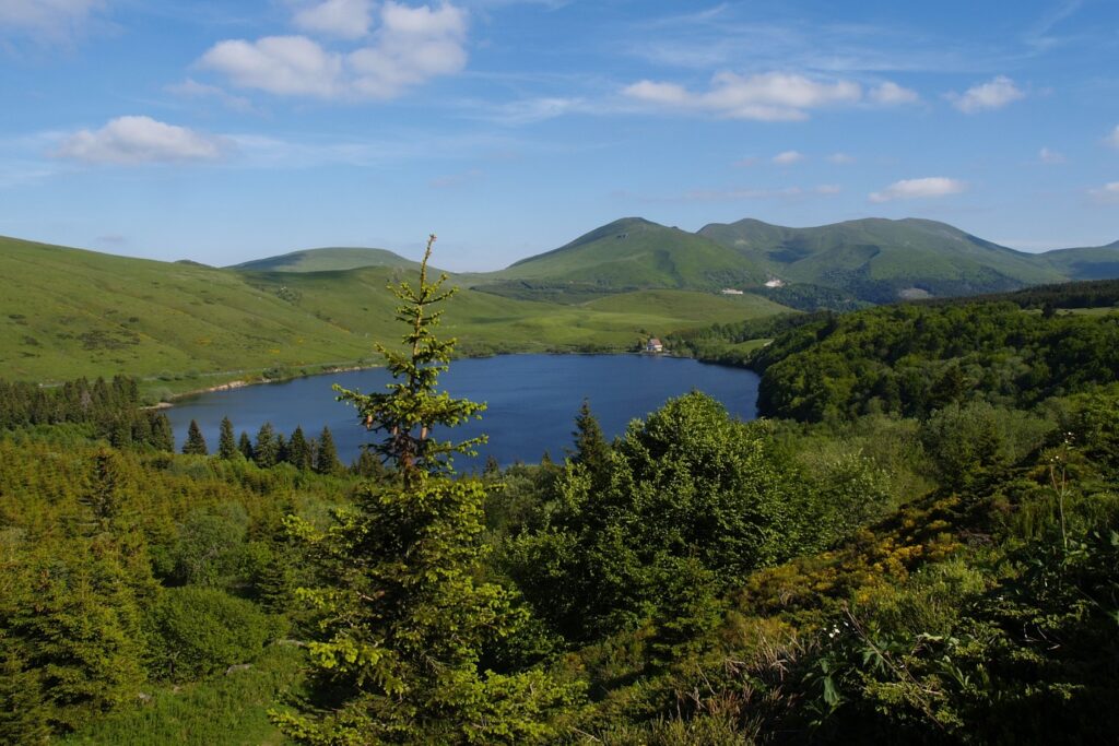 Paysage dans le massif central avec un lac de montagne en contrebas encadré d'arbres et de paysages de montagne