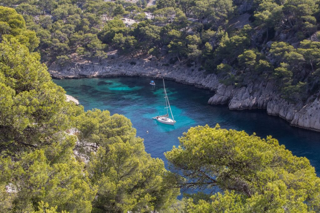 Paysage dans les calangues de Marseille avec en contrebas de l'eau turquoise et un bateau encadré de falaises et d'arbres
