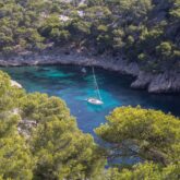 Paysage dans les calangues de Marseille avec en contrebas de l'eau turquoise et un bateau encadré de falaises et d'arbres