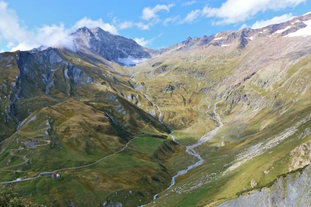 Paysage montagnard avec une cascade d'eau qui part d'un sommet et qui ruisselle à flanc de montagne, avec en fond les sommets