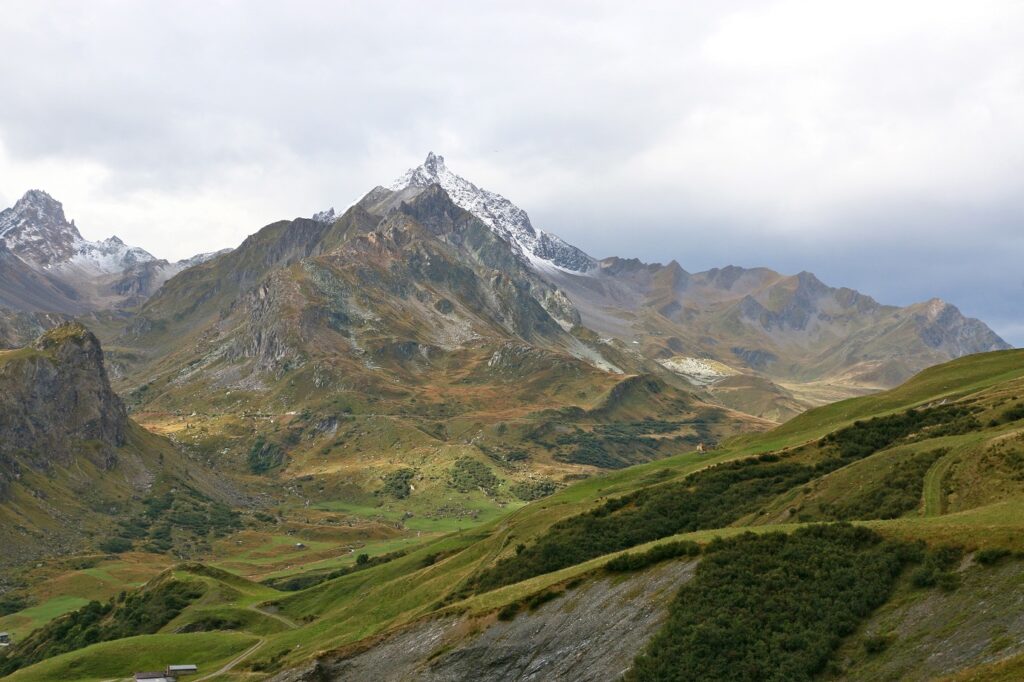 Paysage de montagne avec un sommet enneigé en fond et une vallée de différentes couleurs de vert au premier plan