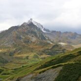 Paysage de montagne avec un sommet enneigé en fond et une vallée de différentes couleurs de vert au premier plan