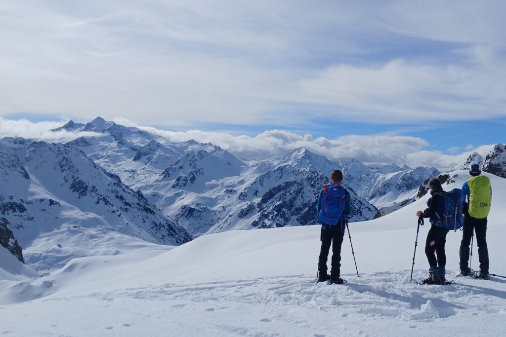 Groupe de randonneurs en raquettes avec leur guide sur un sentier de randonnées en montagne face à la vue