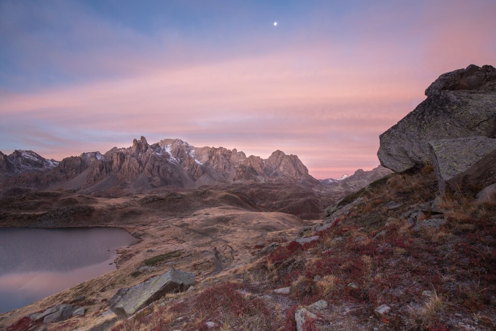 Paysage dans la zone de la commune de Névache au petit matin avec des couleurs rosées dans le ciel et un lac de montagne sur la droite