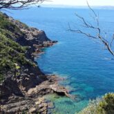 Paysage de littoral avec de l'eau turquoise en contrebas et des rochers de part et d'autre d'une petite crique
