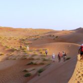 Groupe de randonneurs à Oman sur un sentier à travers les dunes avec leur guide