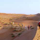 Groupe de randonneurs à Oman sur un sentier à travers les dunes avec leur guide