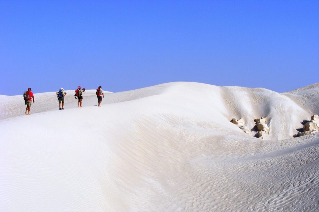 Paysage de sable blanc à Oman avec un groupe de randonneurs et leur guide qui marchent sur les dunes