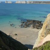 Paysage côtier avec l'eau turquoise sur une plage de sable surplombée par des rochers