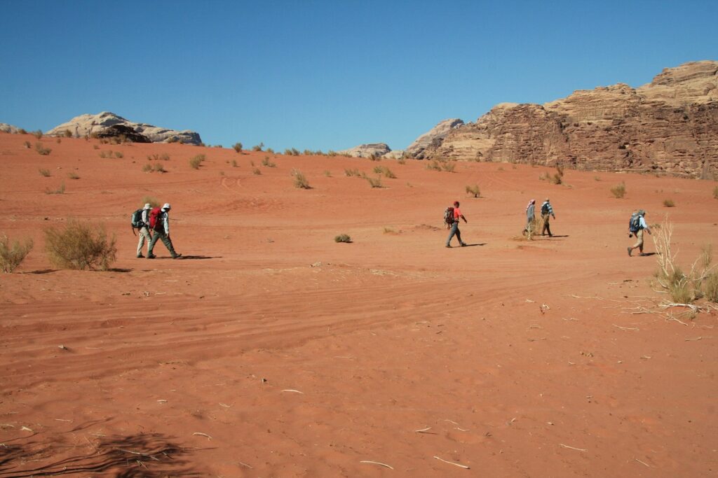 Groupe de randonneurs dans le sable qui marchent en direction de reliefs de montagne en Jordanie