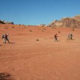 Groupe de randonneurs dans le sable qui marchent en direction de reliefs de montagne en Jordanie