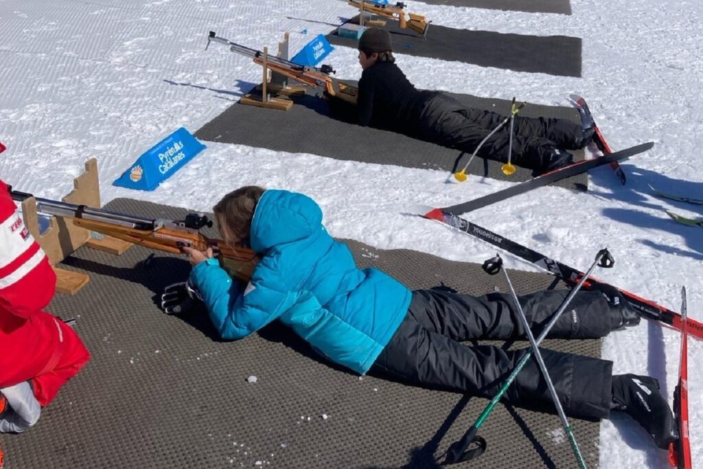 Deux enfants à plat ventre dans la neige sur des stations pour s'entraîner au tir à la carabine, pour s'essayer au biathlon.