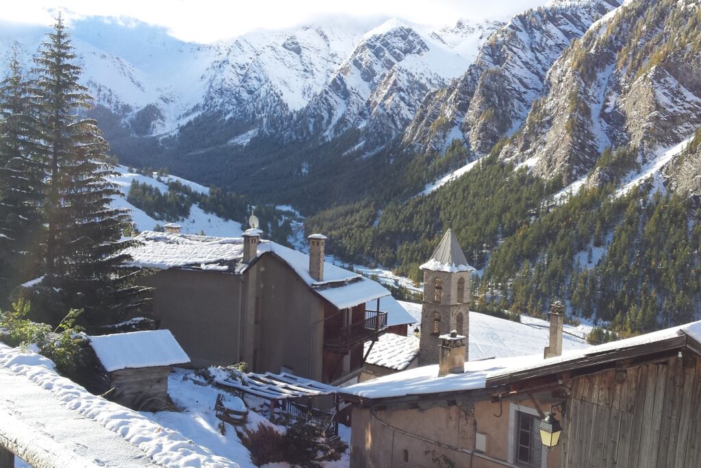 Paysage d'un village enneigé avec une église et des maisons, au fond des sommets, dans le massif du Queyras