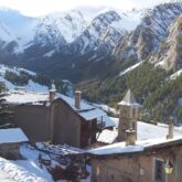 Paysage d'un village enneigé avec une église et des maisons, au fond des sommets, dans le massif du Queyras