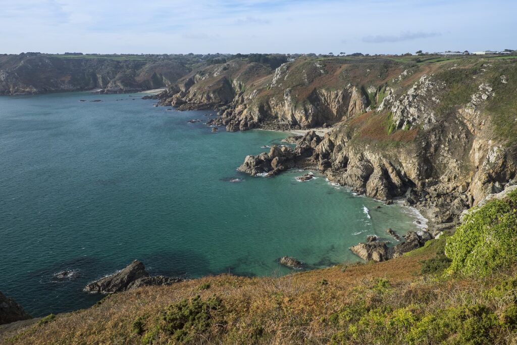 Paysage de littoral encadré de rochers et de falaises avec de l'eau turquoise et transparente.