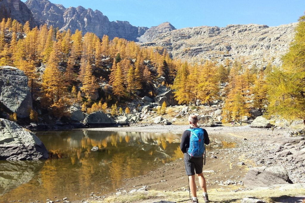 Randonneur face à un lac dans le Mercantour, avec face à lui une forêt surplombée par des montagnes