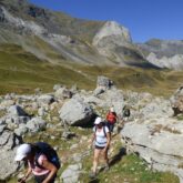 Groupe de randonneurs montant à flanc d'une montagne entre les roches avec différents sommets derrière