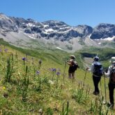 Paysage de montagne avec en fond une crête de montagne et au premier plan un groupe de randonneurs sur un sentier à flanc de montagne