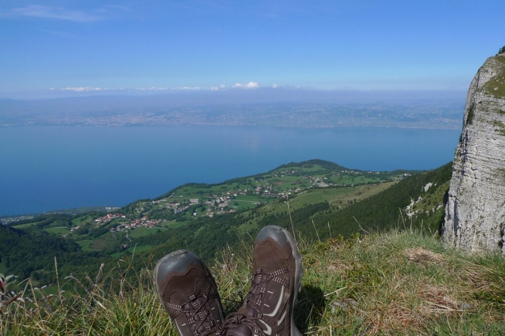 Photo d'un marcheur assis dans l'herbe au sommet d'une montagne avec le lac Léman en contrebas