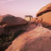 Paysage sur la côte de granit rose en Bretagne avec un bâtiment en fond derrière les rochers du premier plan.