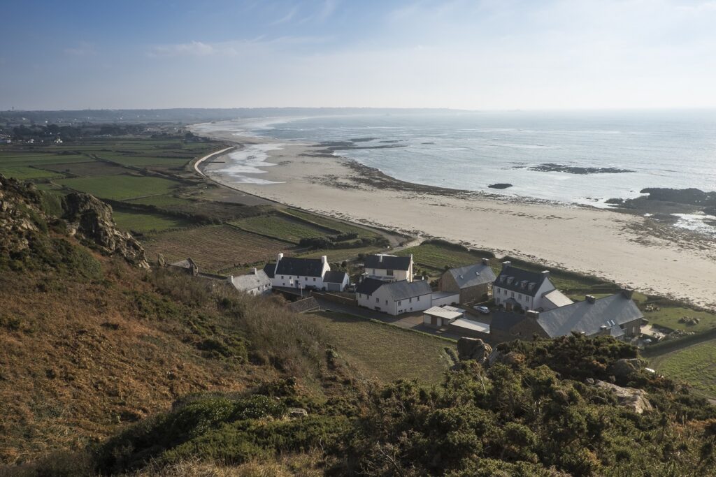 Vue de dessus d'un village avec quelques maisons blanches au toit gris, proche de l'océan, avec une plage pas loin