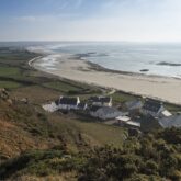 Vue de dessus d'un village avec quelques maisons blanches au toit gris, proche de l'océan, avec une plage pas loin