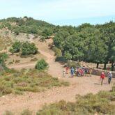Groupe de randonneurs en Sardaigne sur un sentier de randonnée en terre encadré de différents arbres sous un soleil estival