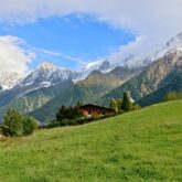 Paysage montagnard avec des sommets en fond et un chalet en bois au premier plan
