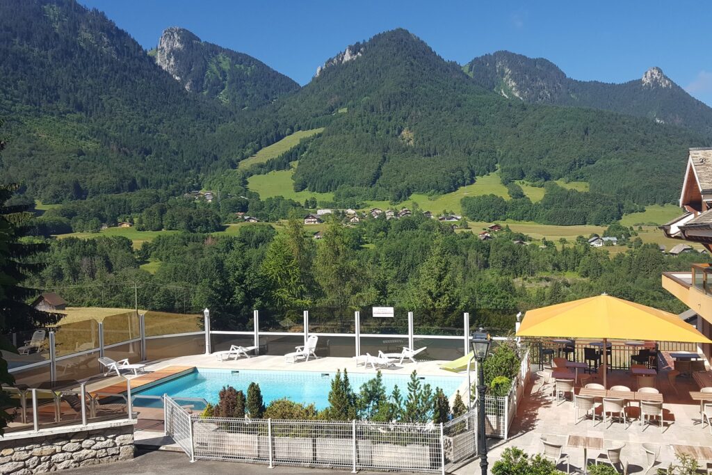Paysage de montagne avec au premier plan la piscine de l'hôtel ainsi que la terrasse de ce dernier, et à l'arrière-plan on y voit différents sommets