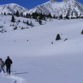Deux randonneurs sur un sentier en raquettes avec leur guide se dirigeant vers des sommets au loin
