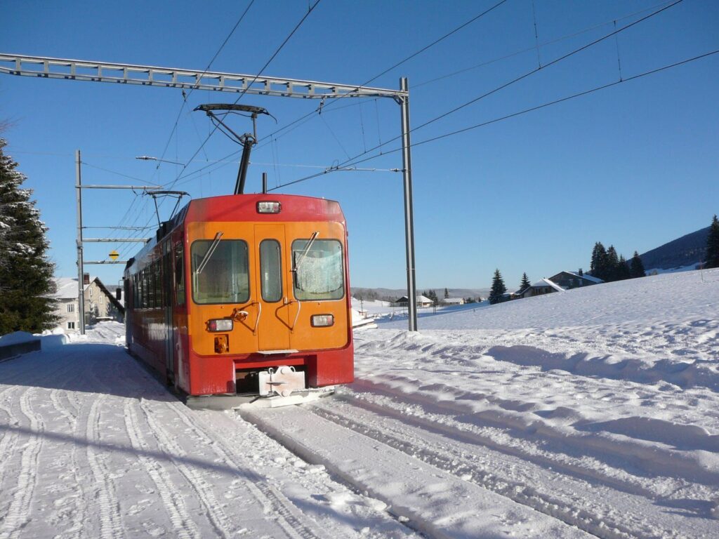 Paysage hivernal du Jura avec un train de couleur rouge et orange